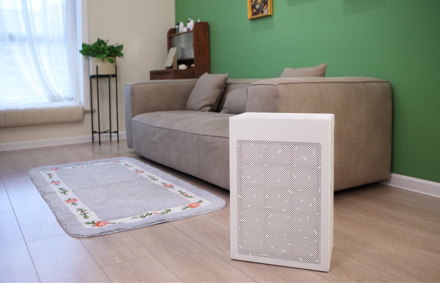 Smart Air SA600 Air purifier on a wooden floor in a living room with a sofa and green wall.