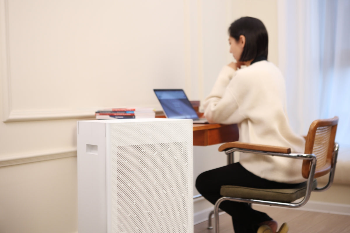 Woman sitting at a desk with a laptop working, next to a Smart Air SA600 air purifier in a room.