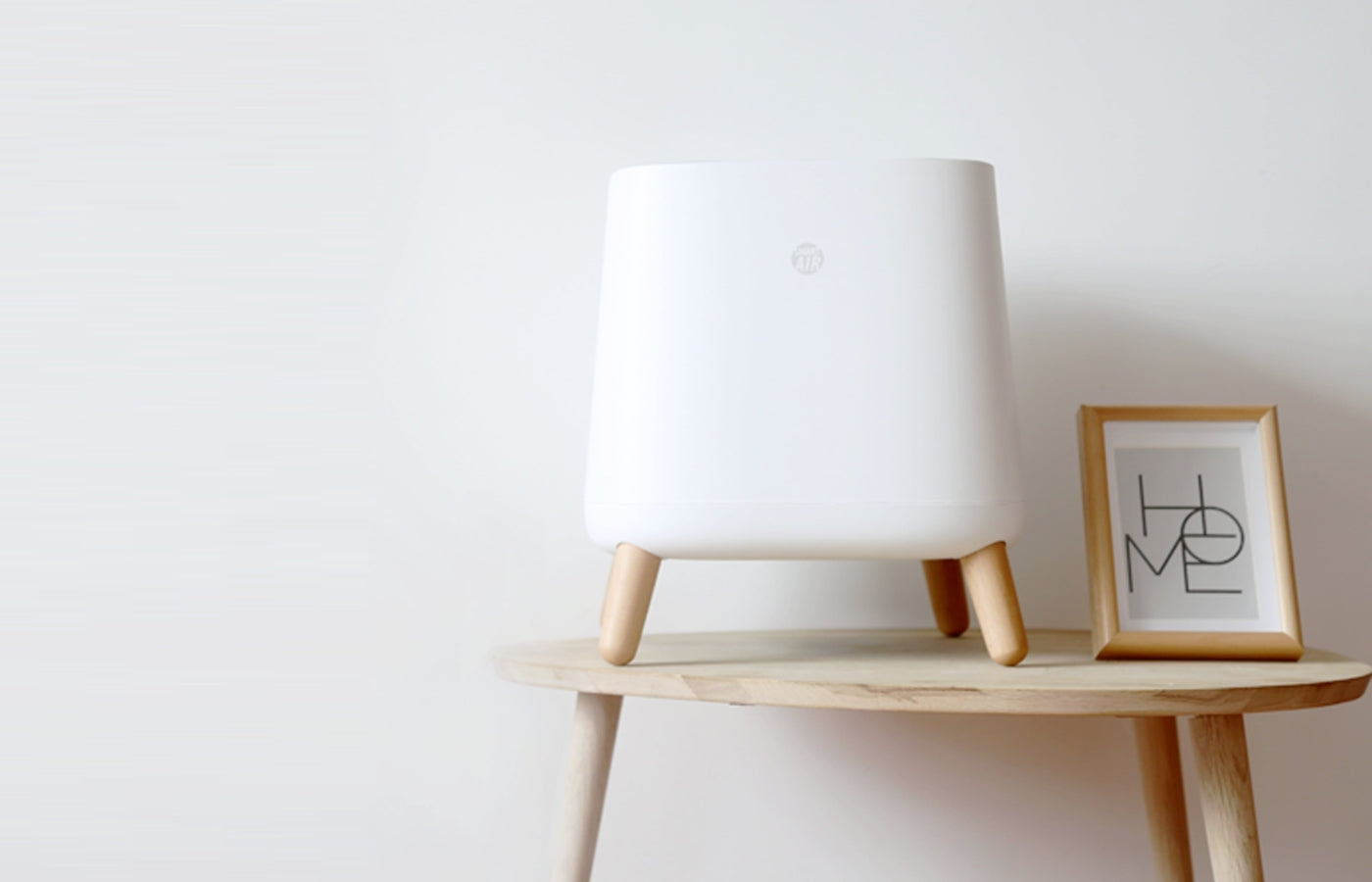 Smart Air Sqair air purifier on a wooden side table with a 'HOME' framed picture against a white wall