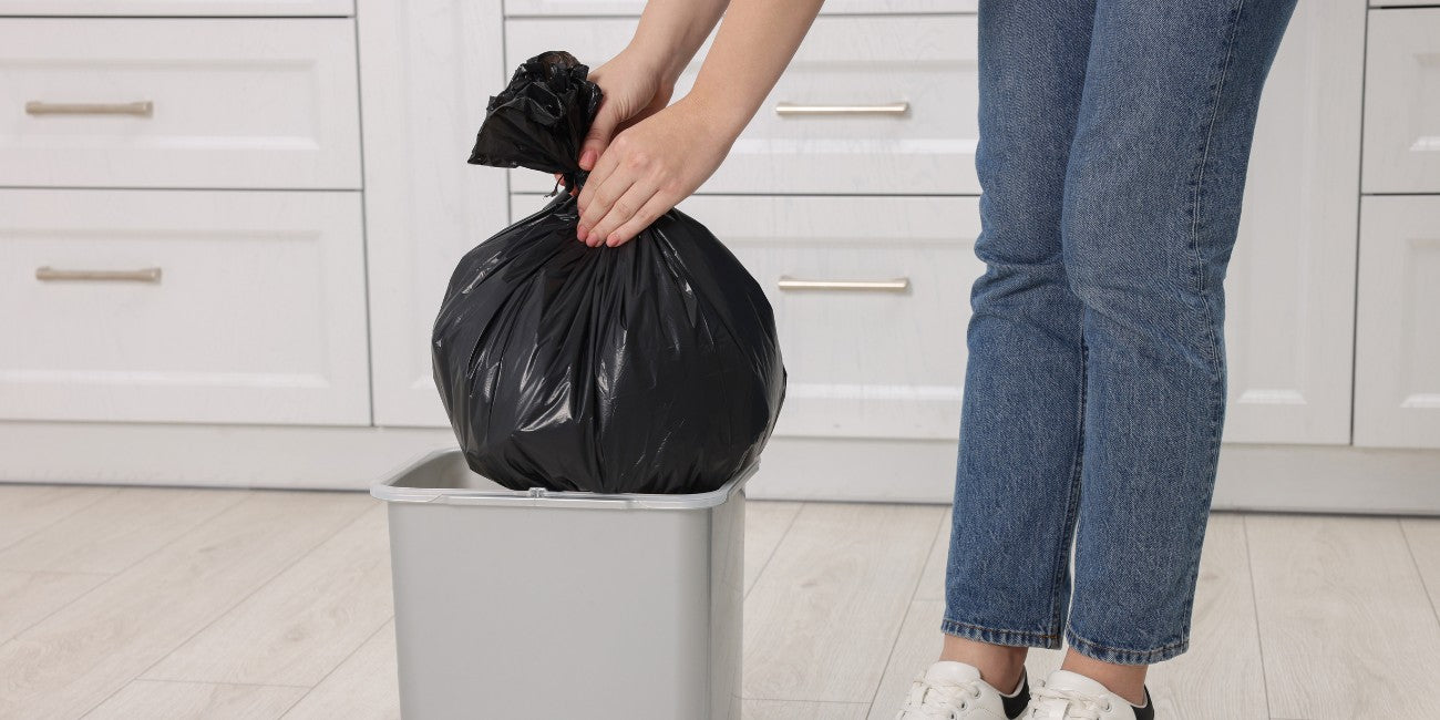 Woman taking rubbish bag out of bin with kitchen drawers in background