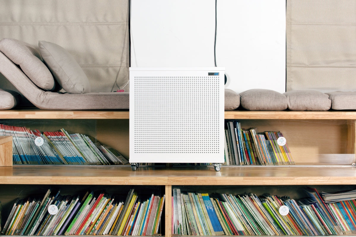 Smart Air blast mini air purifier on a wooden shelf with books and beige cushions in the background