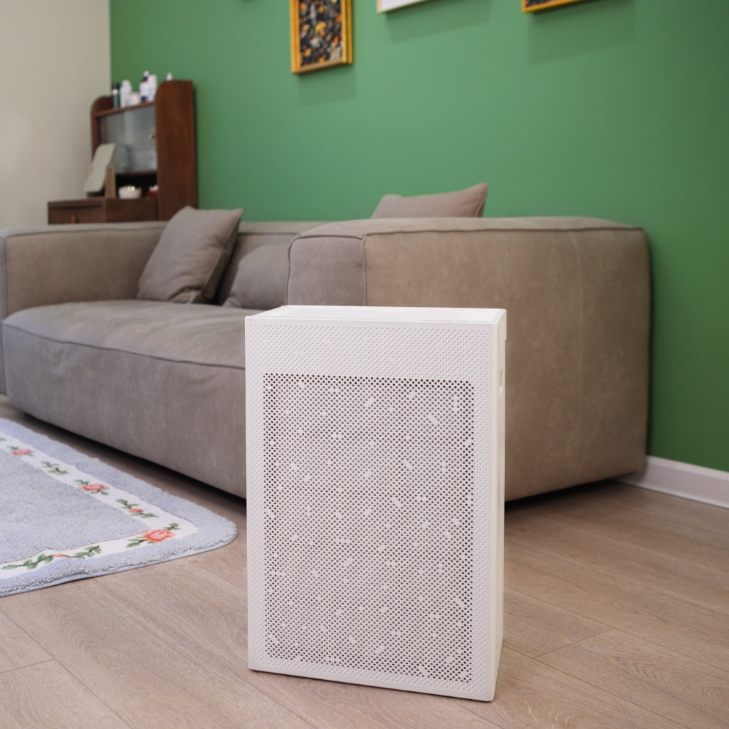 SA600 Air Purifier on wooden floor with grey couch behind it and green wall