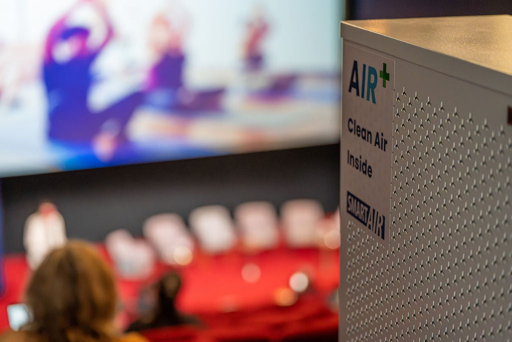 Smart Air purifier labeled 'AIR+ Clean Air Inside' with a blurred background of people and a screen.