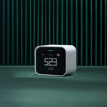QP Lite Air Quality Monitor on a green surface with dark green vertical slat wall in background