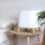 Smart Air Sqair air purifier on wooden table next to a bed with white wall in background